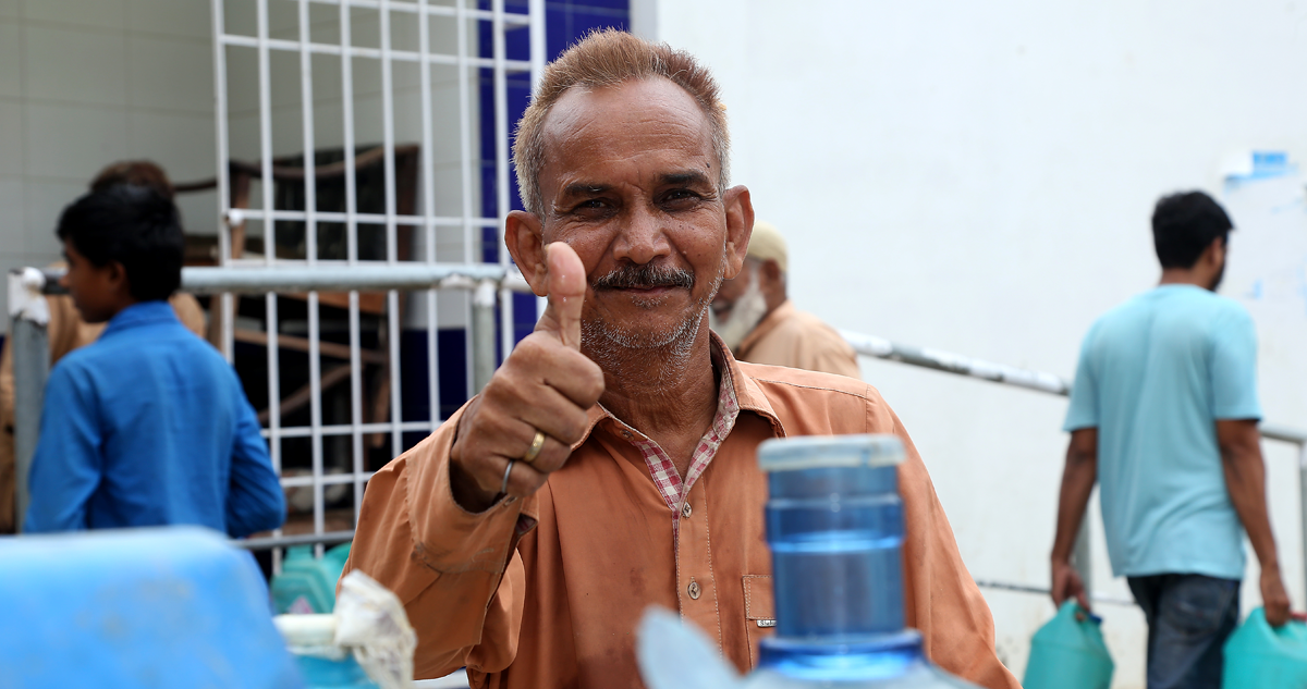 Man holding a thumbs-up near water containers.