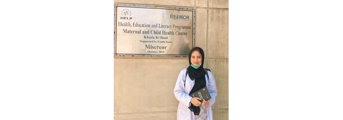 Zehra Batool standing in front of a Misereor Maternal and Child Health Centre sign